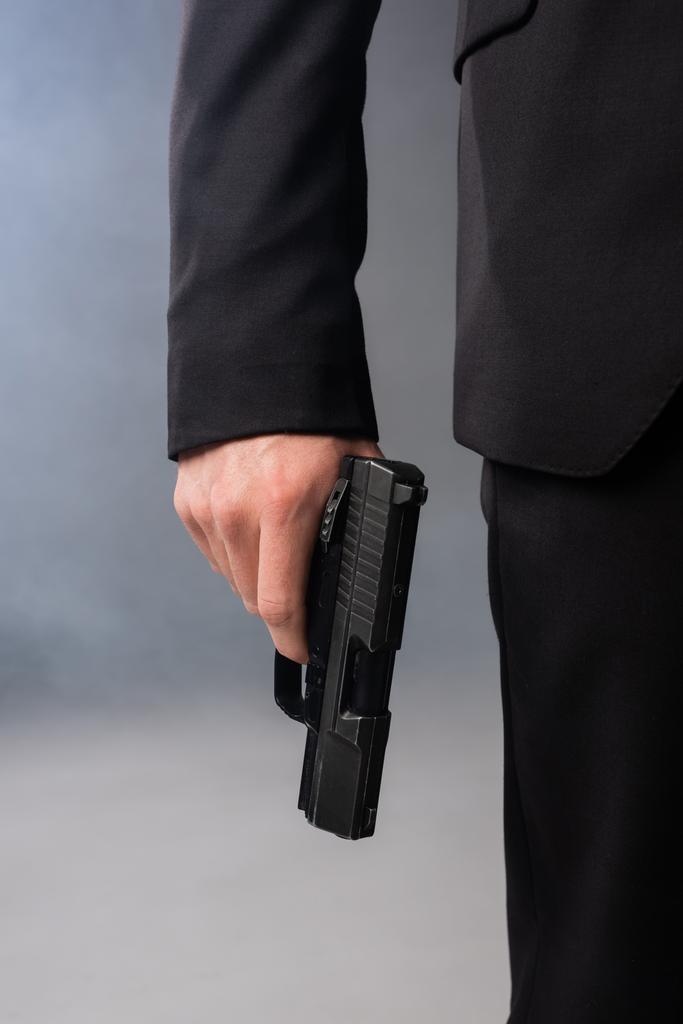 vue recadrée de l'homme d'affaires avec pistolet sur fond gris avec fumée - Photo, image