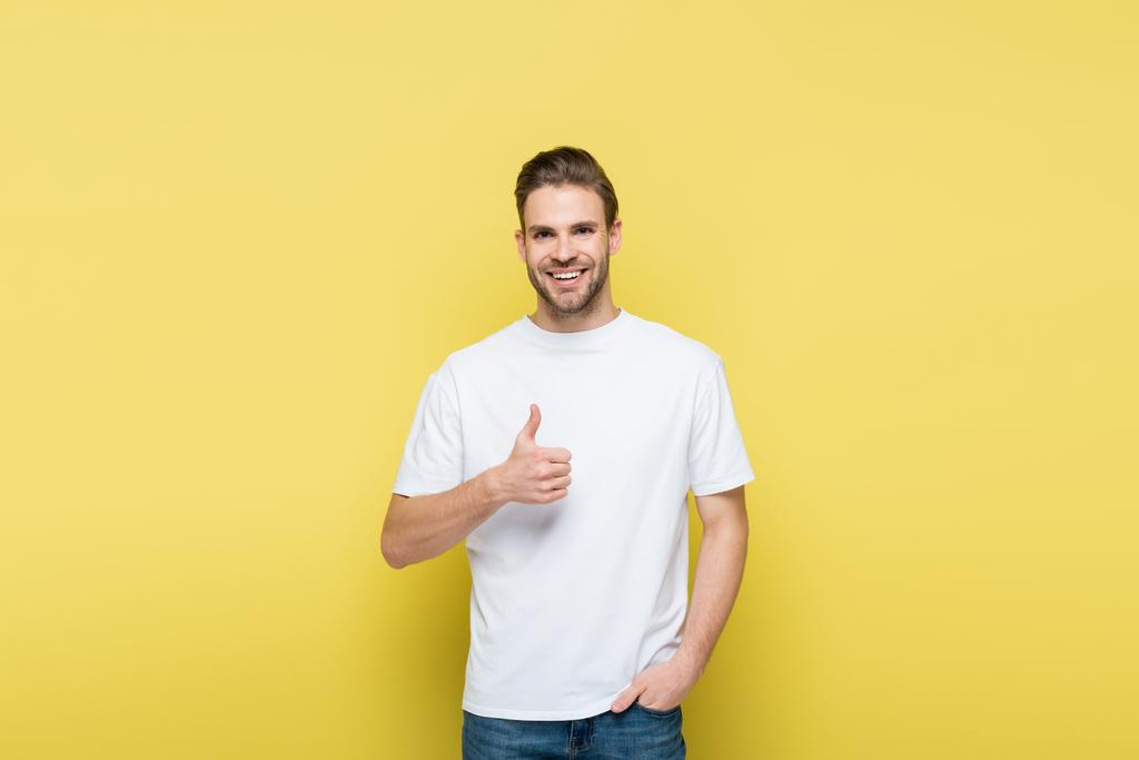 χαμογελαστός άντρας με το χέρι στην τσέπη δείχνει όπως στο κίτρινο - Φωτογραφία, εικόνα
