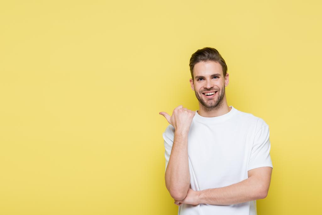joyful man smiling at camera while pointing with thumb on yellow - Photo, Image