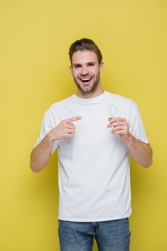 vzrušený muž s otevřenými ústy ukazuje na žárovku na žluté - Fotografie, Obrázek