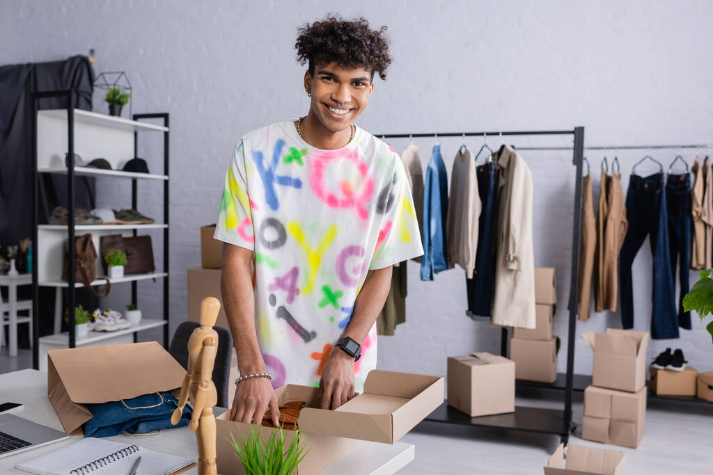 Pozitivní africký americký majitel showroomu uvedení oblečení v kartonové krabici  - Fotografie, Obrázek