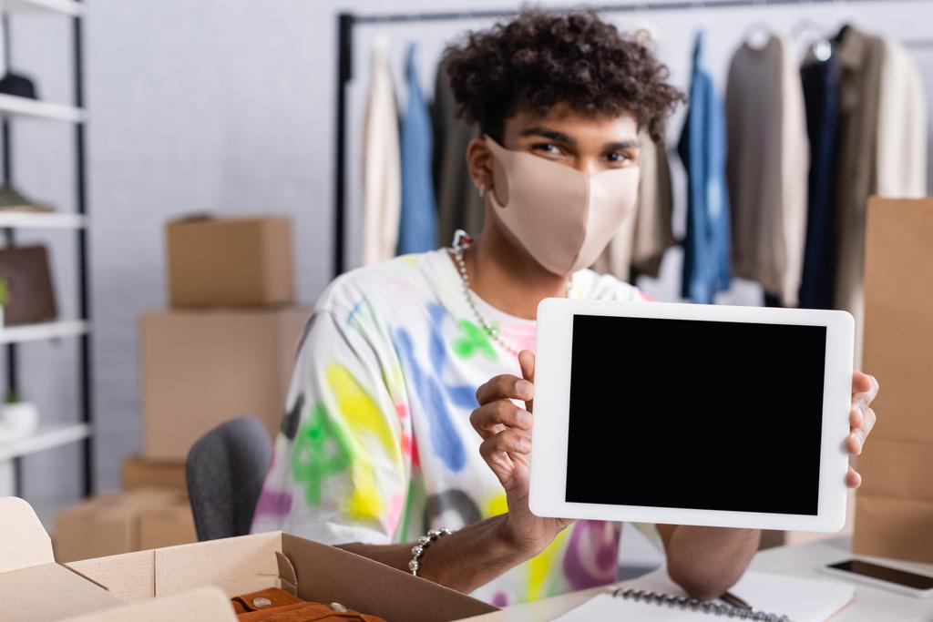 Tableta digital con pantalla en blanco en manos del propietario afroamericano del showroom en máscara protectora  - Foto, imagen