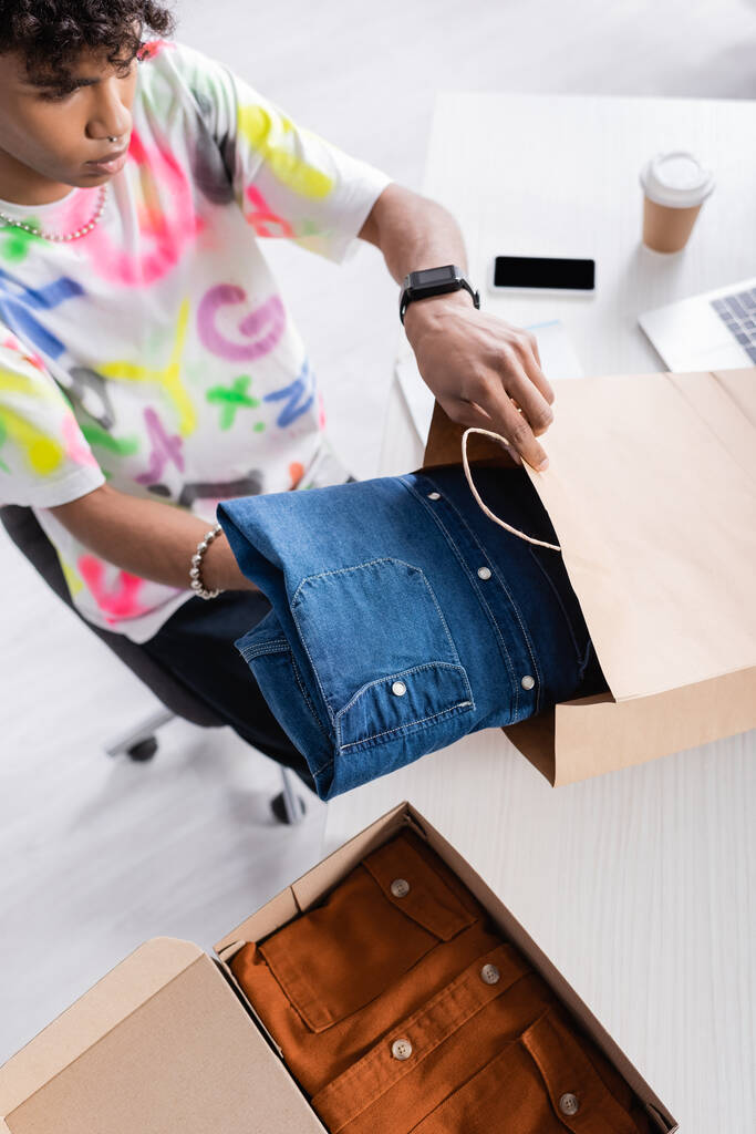 Hoge hoek uitzicht van Afrikaanse Amerikaanse eigenaar van showroom zetten shirt in boodschappentas  - Foto, afbeelding