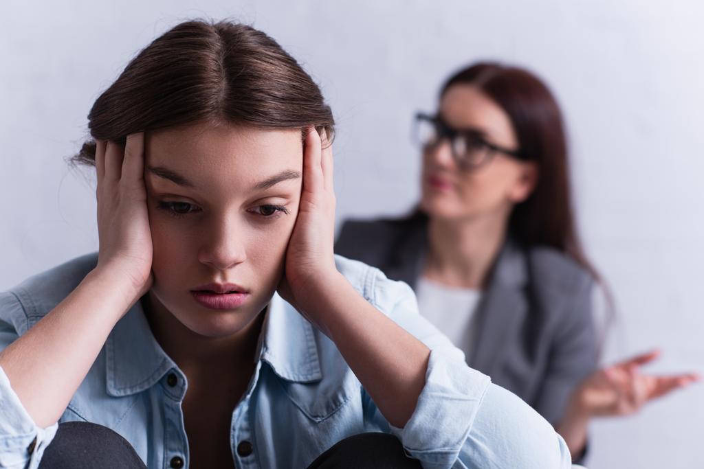 депрессивная девочка-подросток закрывает уши рядом с психологом на размытом фоне  - Фото, изображение