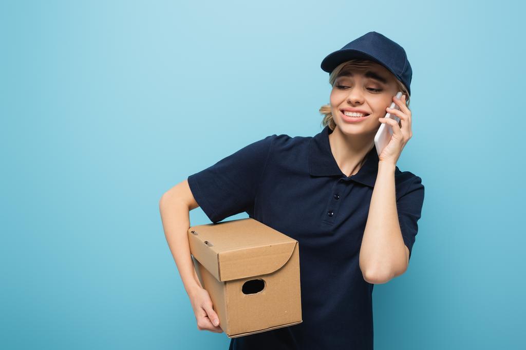 discouraged courier calling on smartphone while holding parcel isolated on blue - Photo, Image