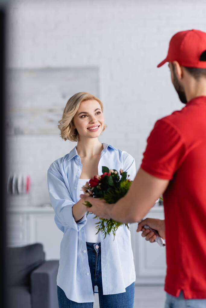 muslim delivery man giving bouquet to joyful woman, blurred foreground - Photo, Image