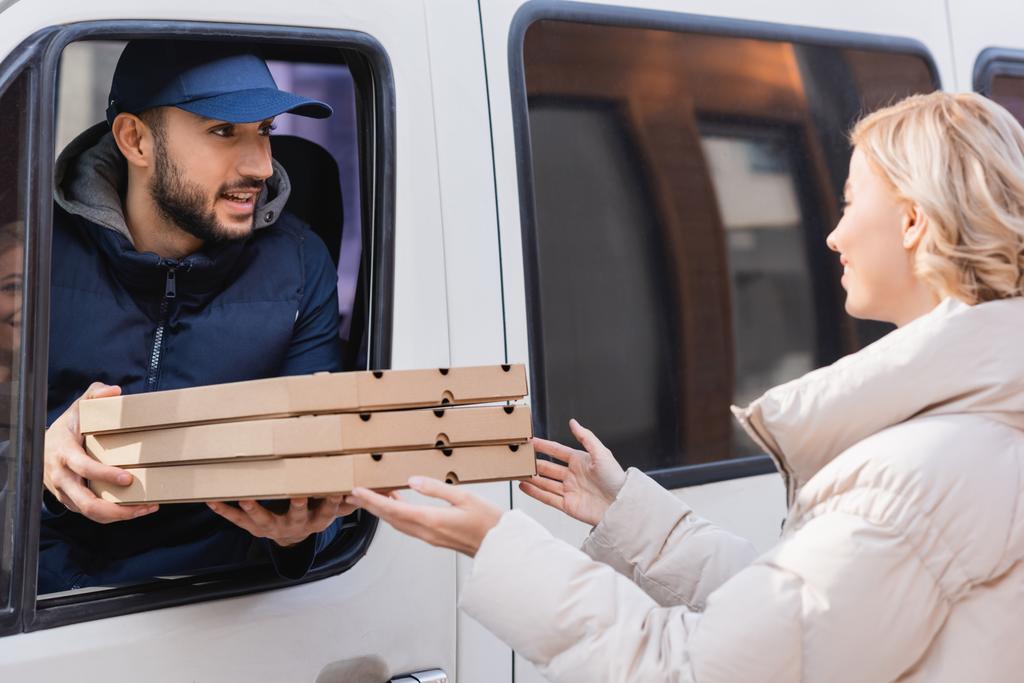 repartidor árabe en camión dando cajas de pizza a mujer rubia - Foto, imagen