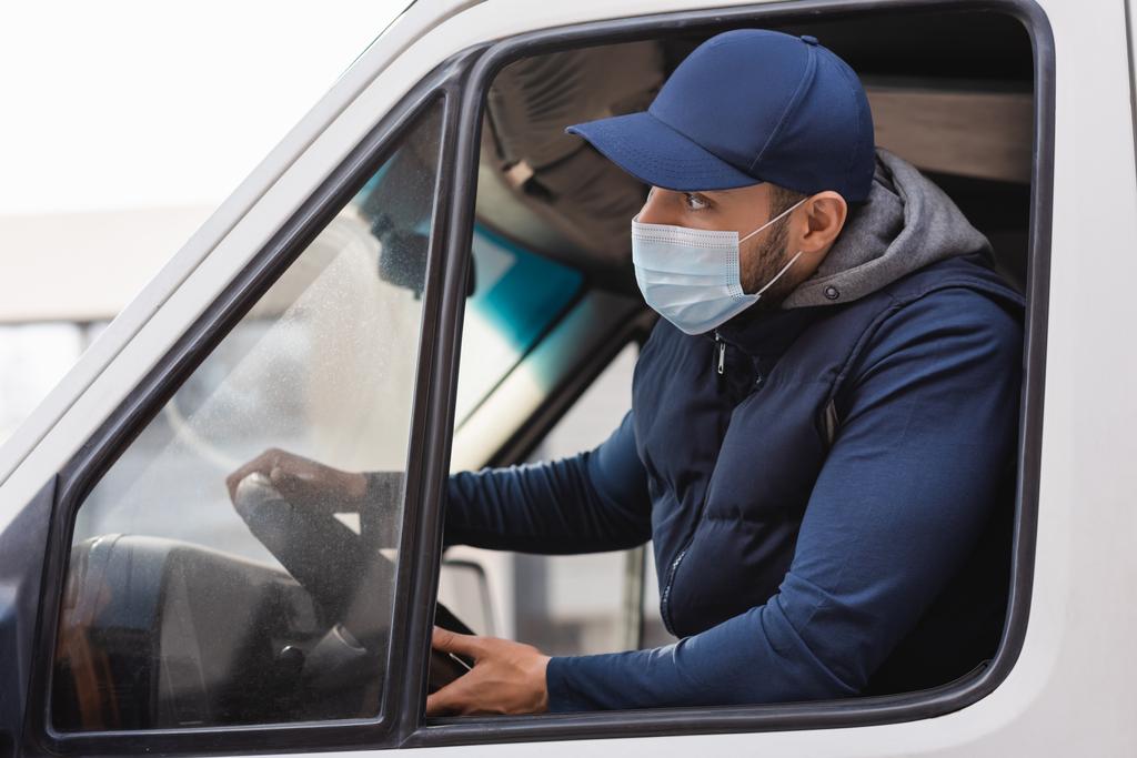 Arabo uomo consegna in maschera medica guardando avanti durante la guida di camion - Foto, immagini