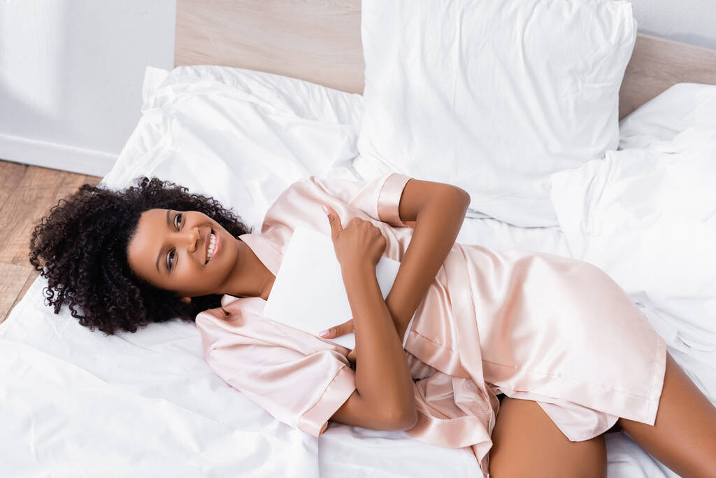 Nagy látószögű kilátás mosolygós afro-amerikai nő ölelés digitális tabletta az ágyban  - Fotó, kép