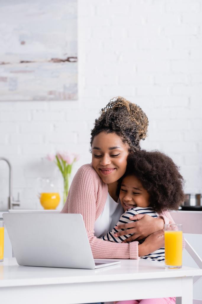 boldog afro-amerikai anya átöleli lánya, miközben filmet nézni laptop reggeli közben - Fotó, kép
