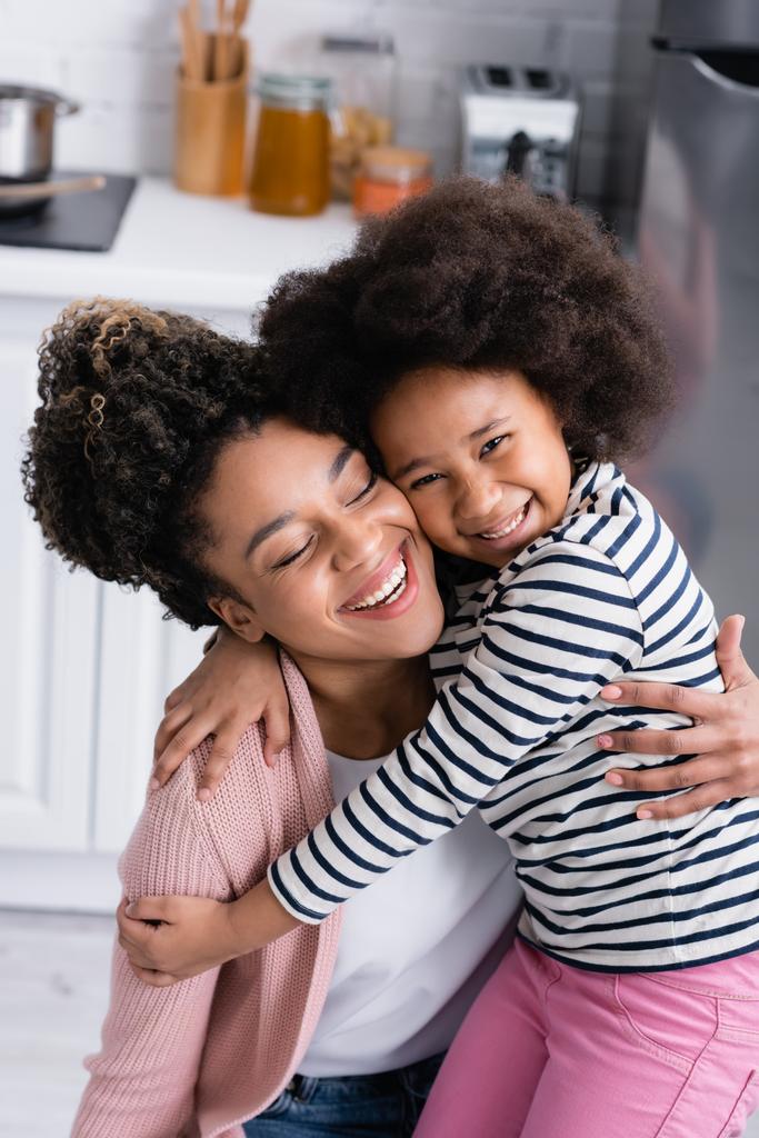 boldog afro-amerikai nő átöleli vidám gyermek a konyhában - Fotó, kép
