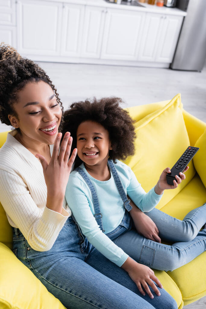 excited african american mother and daughter watching movie on sofa at home - Photo, Image