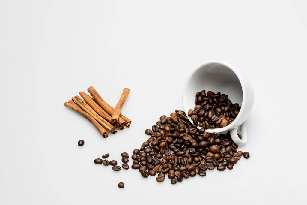 корица палочки возле чашки с кофейными зёрнами на белом - Фото, изображение
