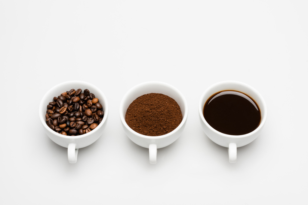 Tassen mit vorbereitetem und gemahlenem Kaffee in der Nähe von Bohnen auf weiß - Foto, Bild
