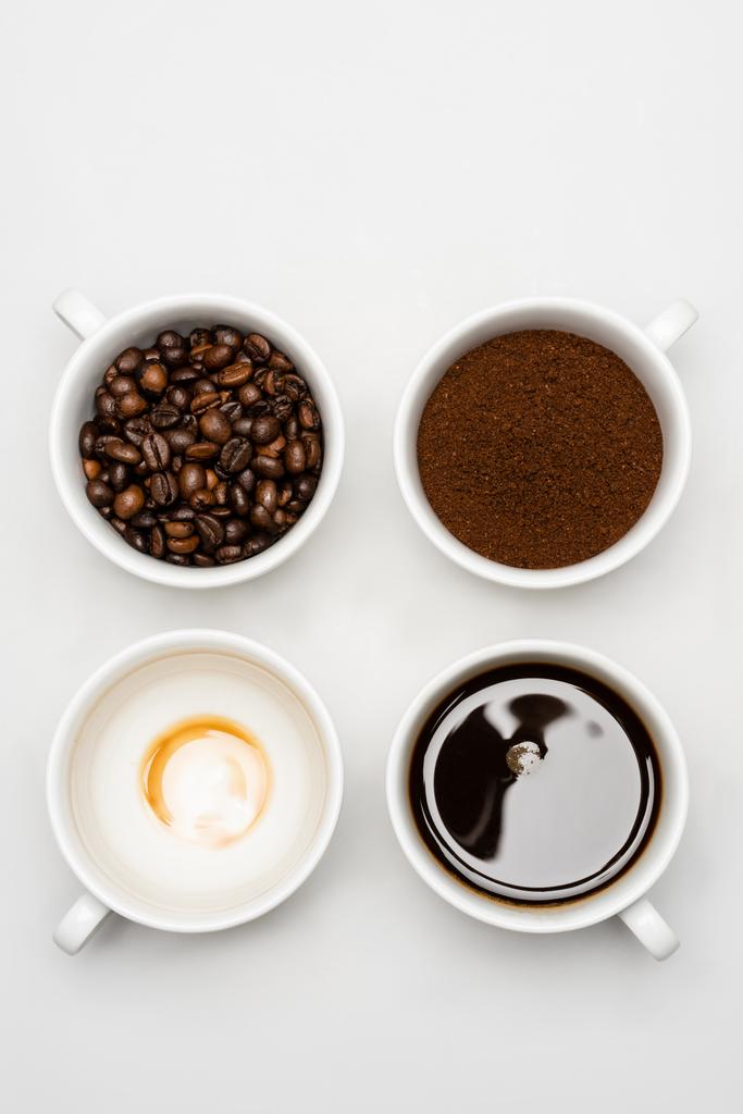 вид сверху на приготовленный американо возле свежего молотого кофе и бобы в чашках на белом - Фото, изображение