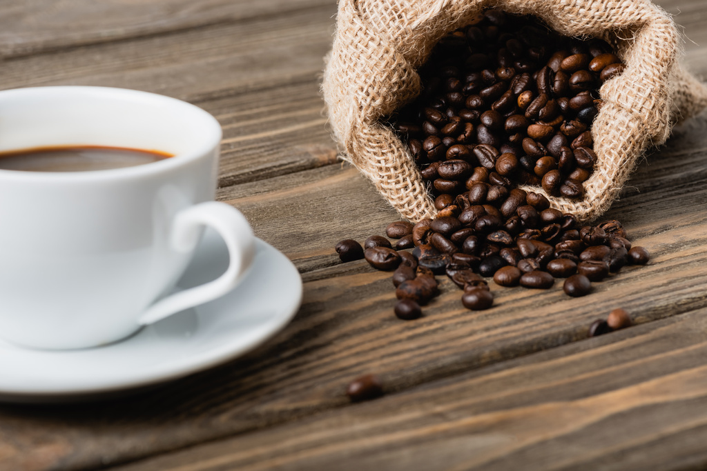ваянський мішок з смаженими кавовими зернами біля чашки на розмитому передньому плані
  - Фото, зображення