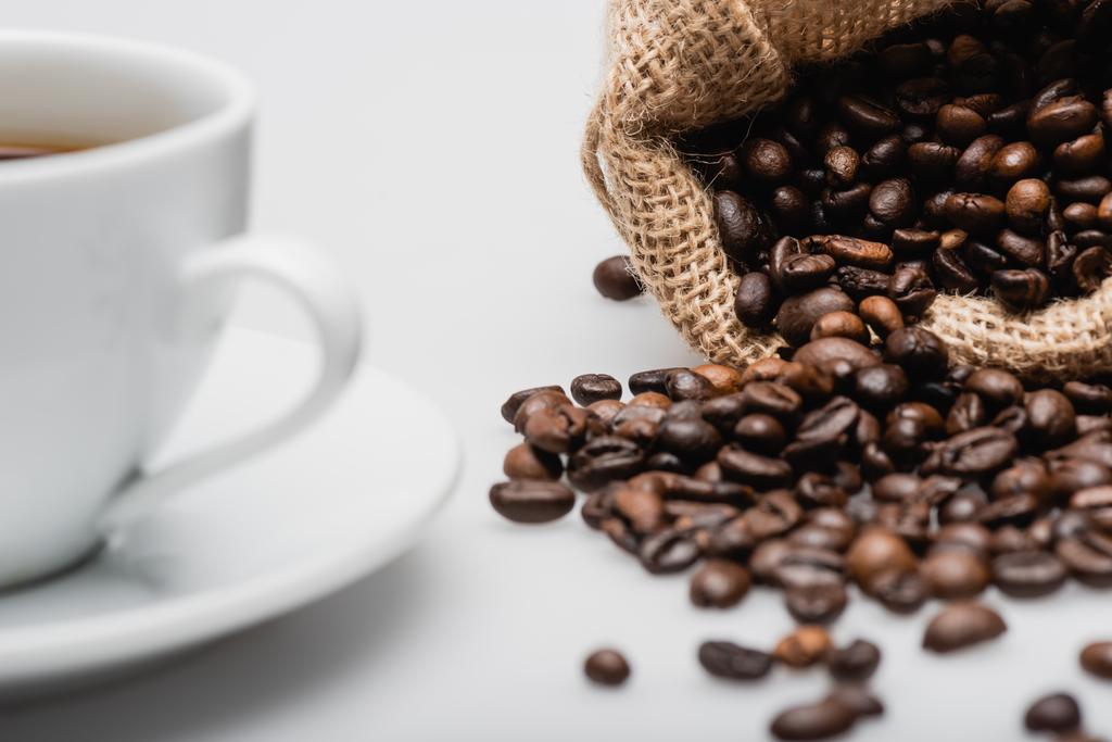 zsákzsák pörkölt kávébabbal csésze közelében elmosódott előtérben  - Fotó, kép