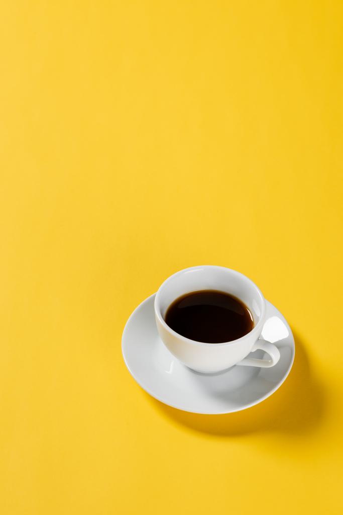 high angle view of black coffee in white cup on yellow background  - Photo, Image