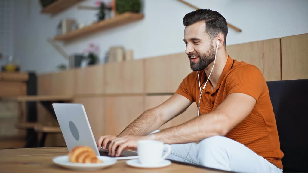 wesoły człowiek słuchający muzyki w słuchawkach i korzystający z laptopa w kawiarni - Zdjęcie, obraz
