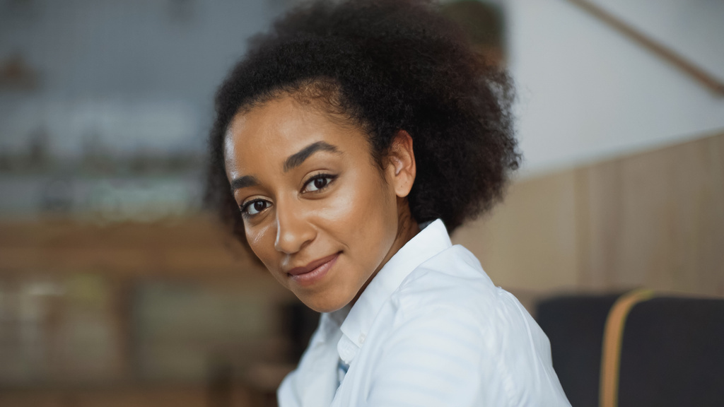 Радостная африканская американка улыбается и смотрит в камеру в кафе - Фото, изображение