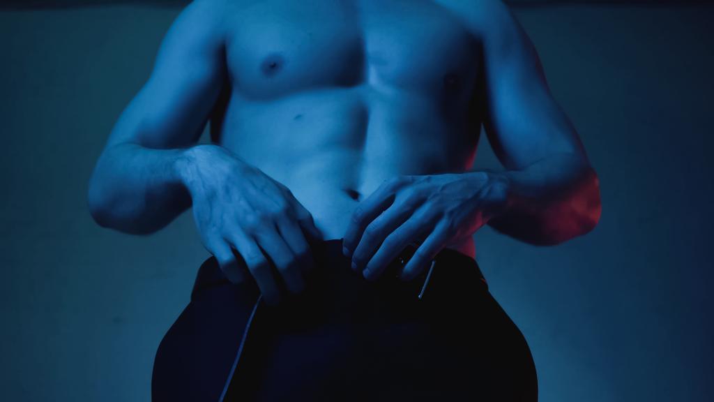 vista ritagliata di uomo sexy e muscoloso spogliarsi sul blu - Foto, immagini
