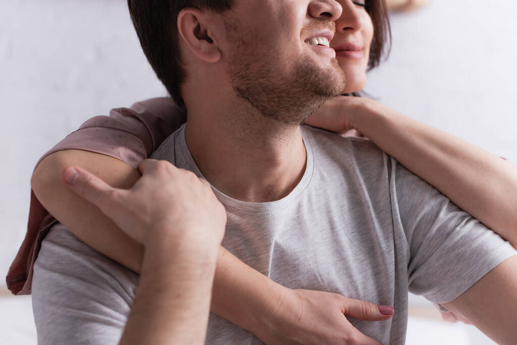 Обрезанный вид улыбающегося мужчины касающегося руки жены на размытом фоне  - Фото, изображение