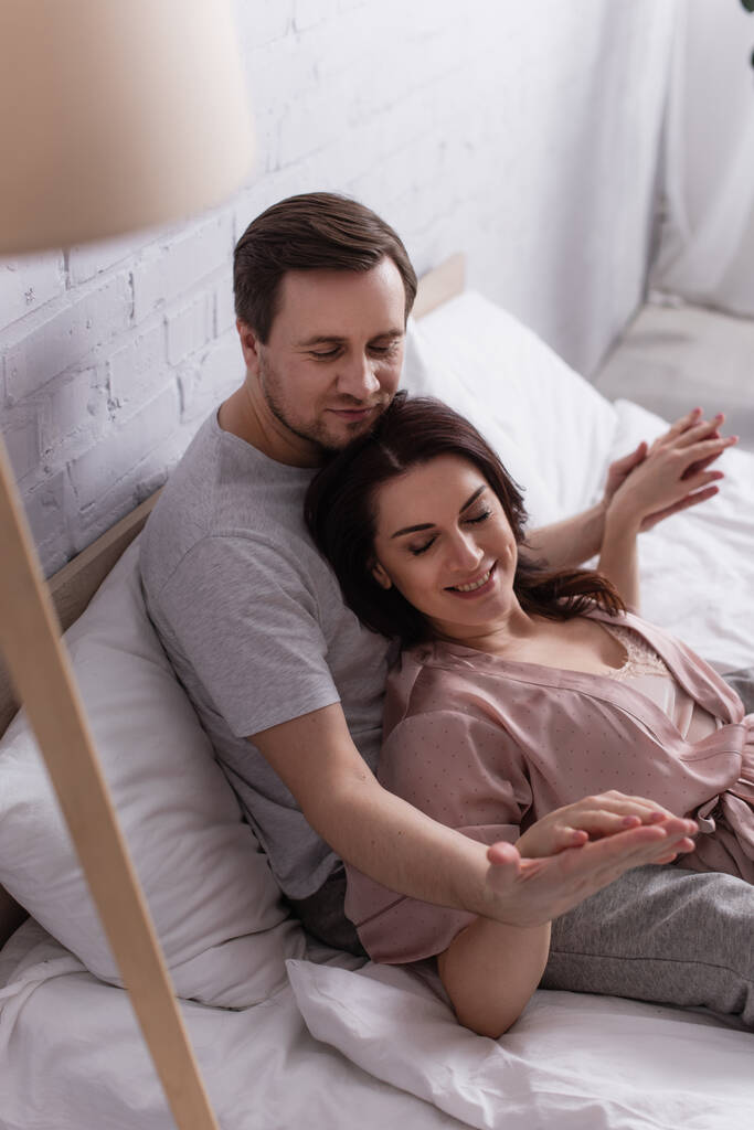 Мужчина смотрит на руку улыбающейся жены на кровати  - Фото, изображение