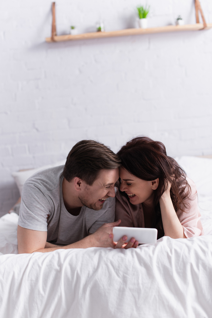 Alegre pareja adulta con smartphone acostado en la cama  - Foto, imagen