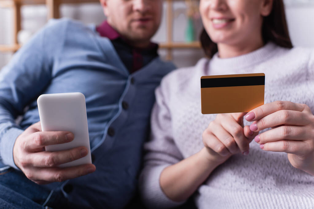 Vista cortada de celular e cartão de crédito em mãos de casal em fundo embaçado  - Foto, Imagem