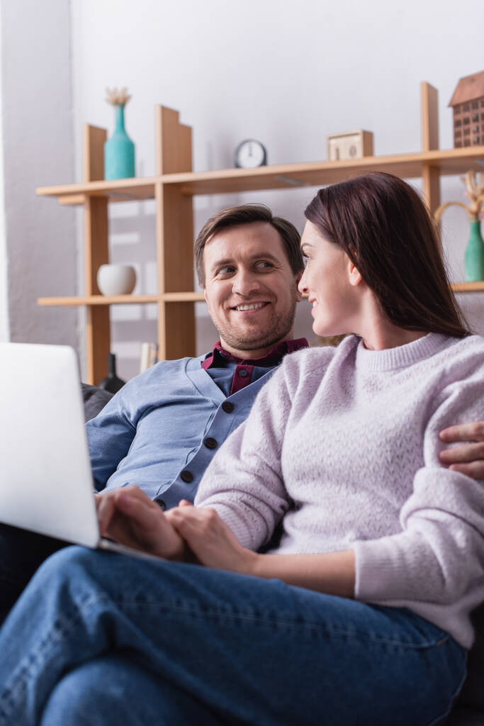 glimlachende man knuffelen vrouw met laptop op wazig voorgrond  - Foto, afbeelding