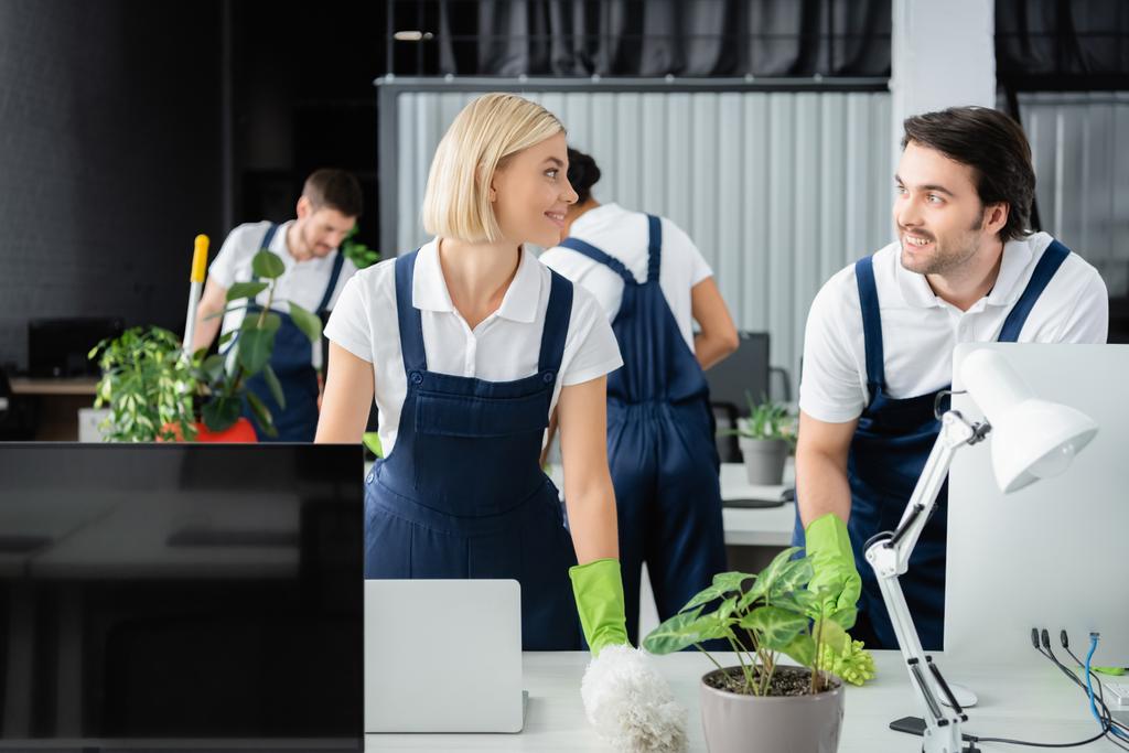 Smiling cleaners talking near table with computers in office  - Photo, Image
