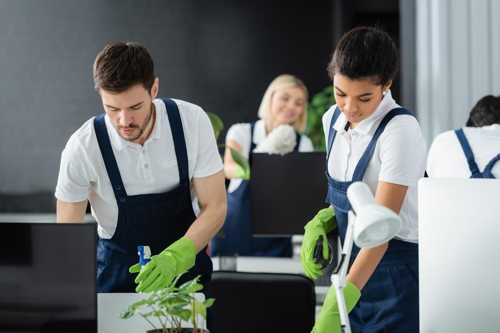 Interracial cleaners with detergents working near computers in office  - Photo, Image