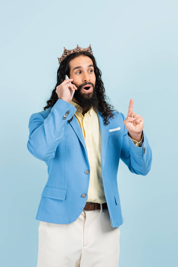 здивований іспаномовний чоловік в куртці і короні розмовляє на смартфоні ізольовано на синьому
 - Фото, зображення