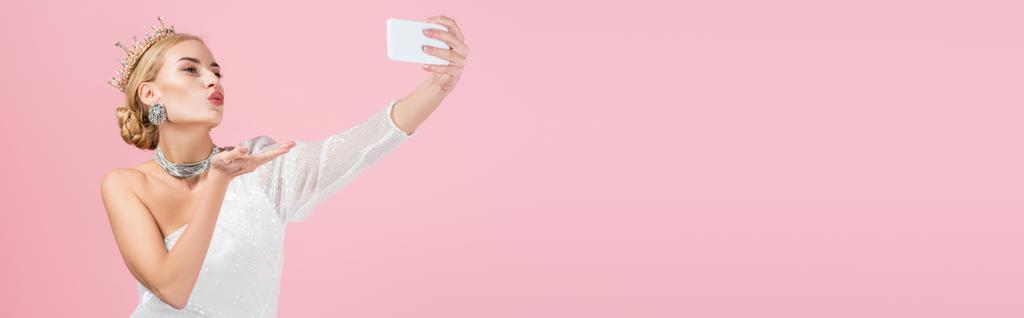 blondynka w luksusowej koronie robi selfie na smartfonie i wysyła pocałunek powietrza odizolowany na różowy, baner - Zdjęcie, obraz