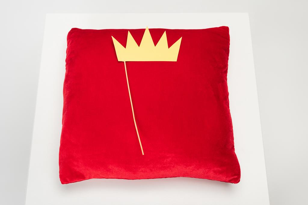 vue du dessus de la couronne en papier jaune sur bâton et oreiller en velours rouge sur gris - Photo, image
