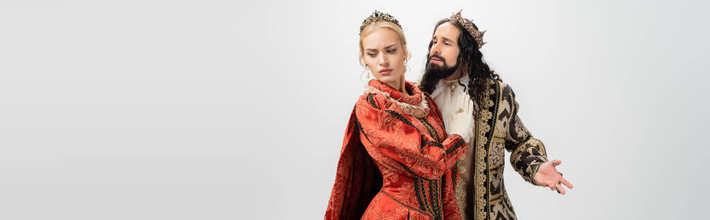 rey y reina interracial en ropa medieval y coronas aisladas en blanco, bandera - Foto, Imagen