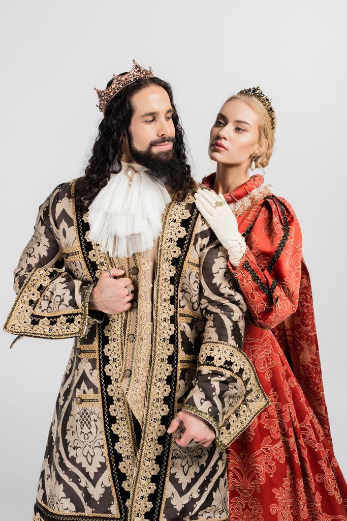 Blonde Königin in königlicher Krone umarmt hispanischen König in mittelalterlicher Kleidung isoliert auf weiß - Foto, Bild