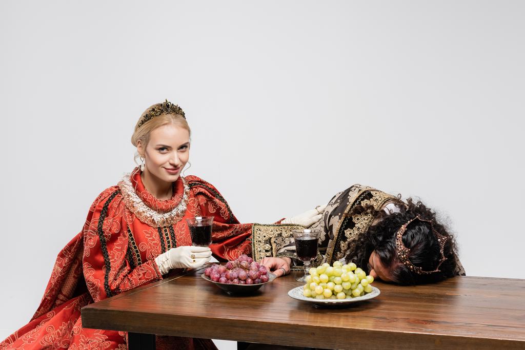 щаслива королева тримає келих червоного вина біля отруєного його короля в середньовічному одязі ізольовані на білому
 - Фото, зображення