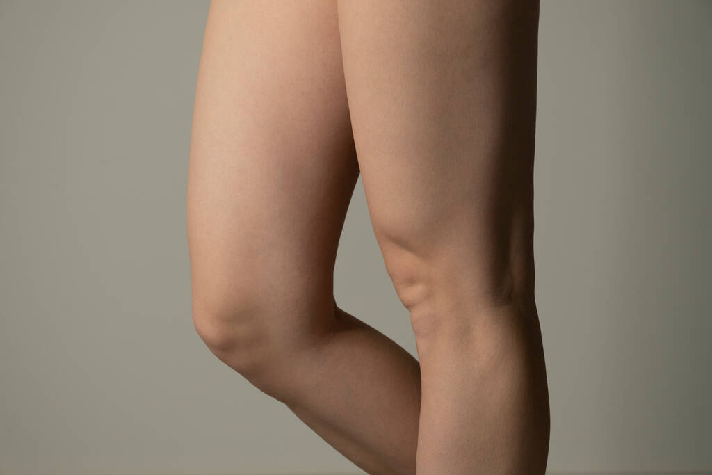 Толстые ноги, вид сбоку - тощая толстая фигура. Женские бёдра крупным планом снимают студию на сером фоне. Диета и потеря жира. - Фото, изображение