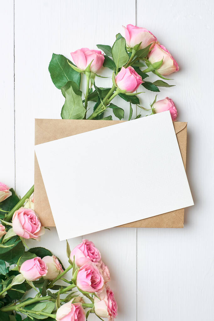 Carte de voeux avec enveloppe et roses fraîches sur fond blanc, maquette avec espace de copie - Photo, image