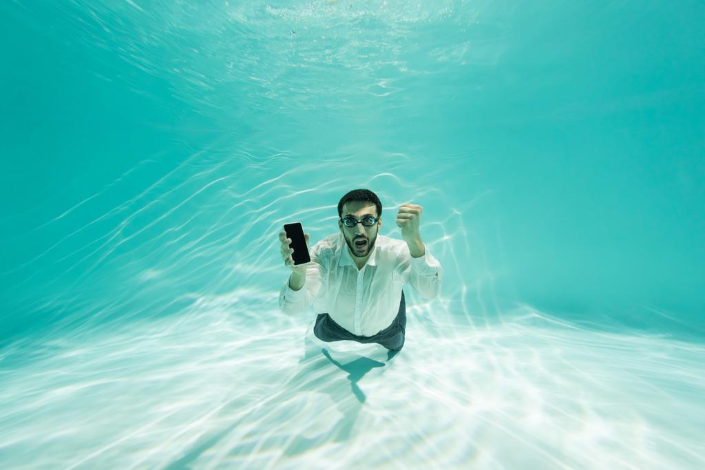 Muzułmański biznesmen w goglach trzyma smartfona i pokazuje tak gest pod wodą  - Zdjęcie, obraz
