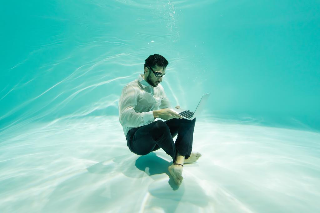 Аравійський бізнесмен використовує ноутбук під водою в басейні.  - Фото, зображення