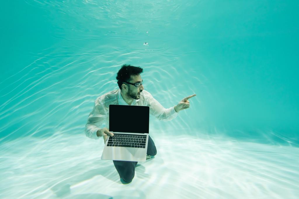 Arabischer Geschäftsmann zeigt mit Finger und hält Laptop im Swimmingpool  - Foto, Bild