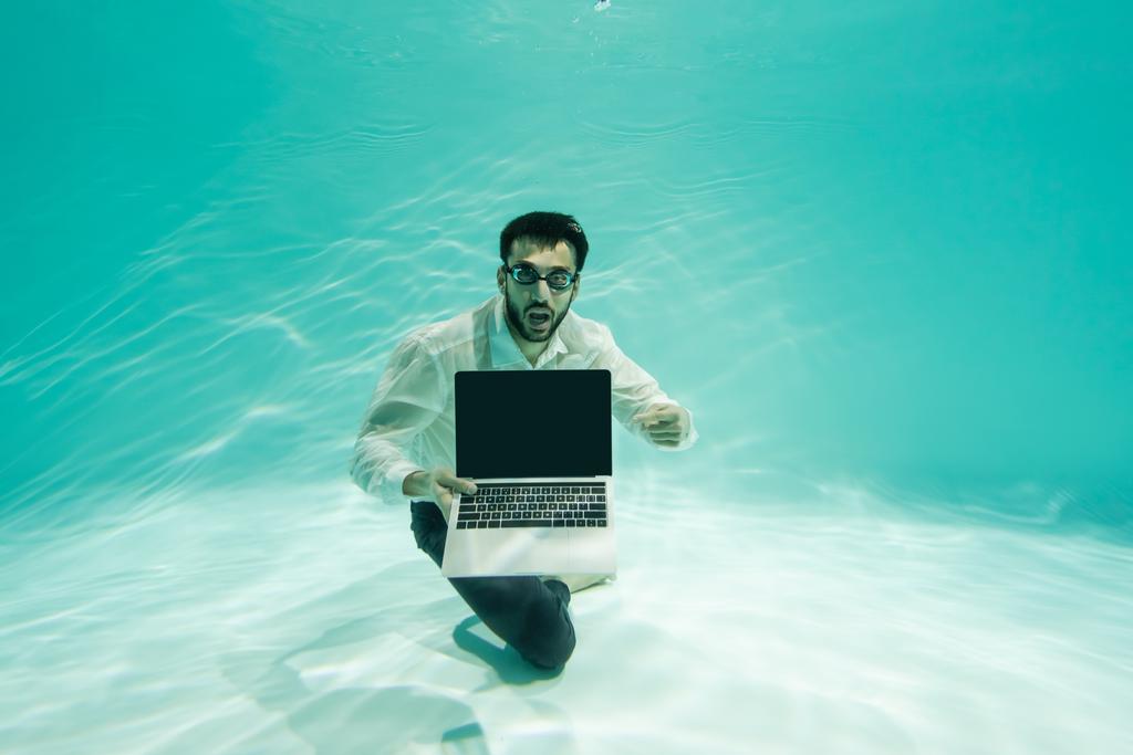 Verbazingwekkende Arabische zakenman wijst naar laptop met leeg scherm onder water in het zwembad  - Foto, afbeelding