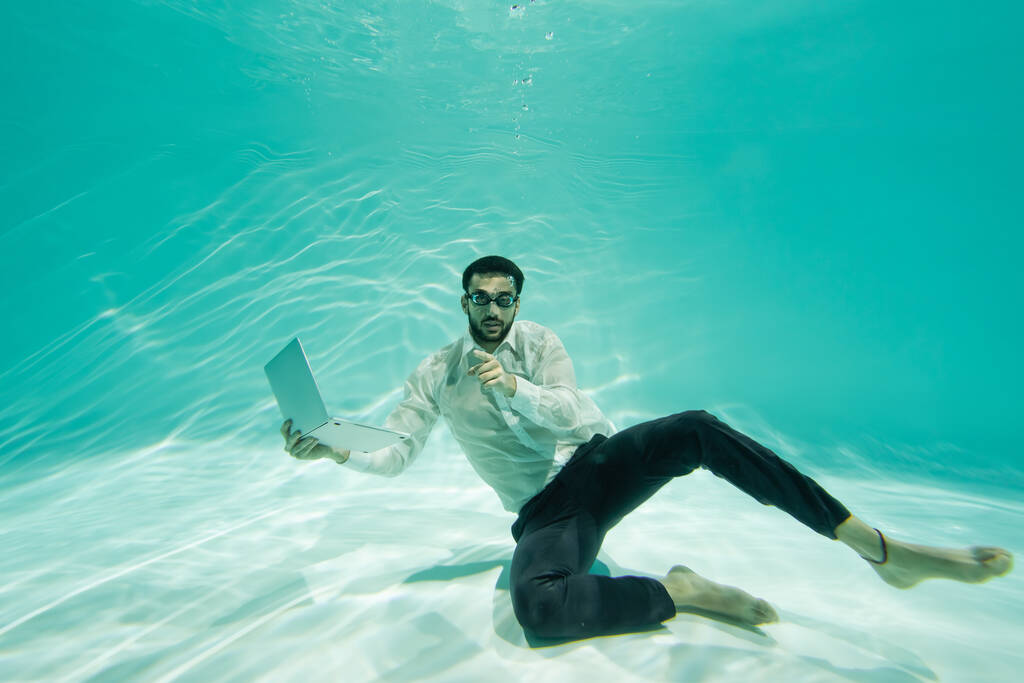 Muslimský podnikatel ukazuje prstem, zatímco drží notebook v bazénu  - Fotografie, Obrázek