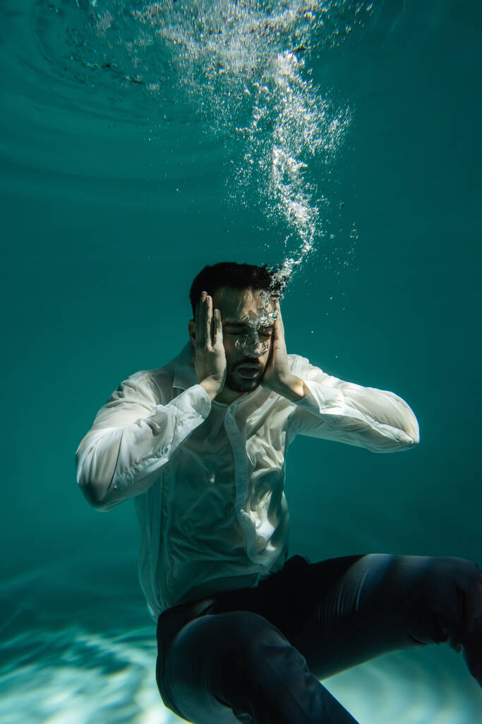 Arabo uomo d'affari con le mani vicino alla testa nuotare sott'acqua in piscina  - Foto, immagini