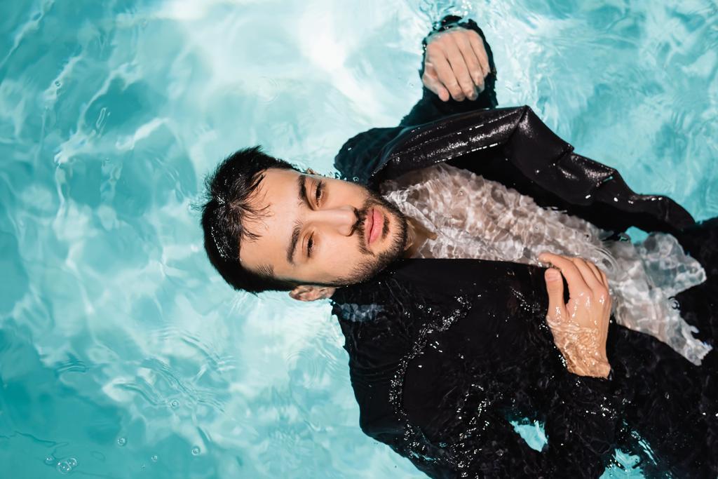 Κάτοψη του αραβικού επιχειρηματία με κοστούμι που κολυμπά στην πισίνα με φως  - Φωτογραφία, εικόνα