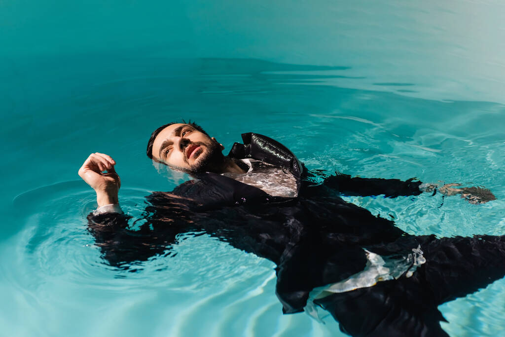 Arabische zakenman in formele kleding kijken weg tijdens het zwemmen in het zwembad  - Foto, afbeelding