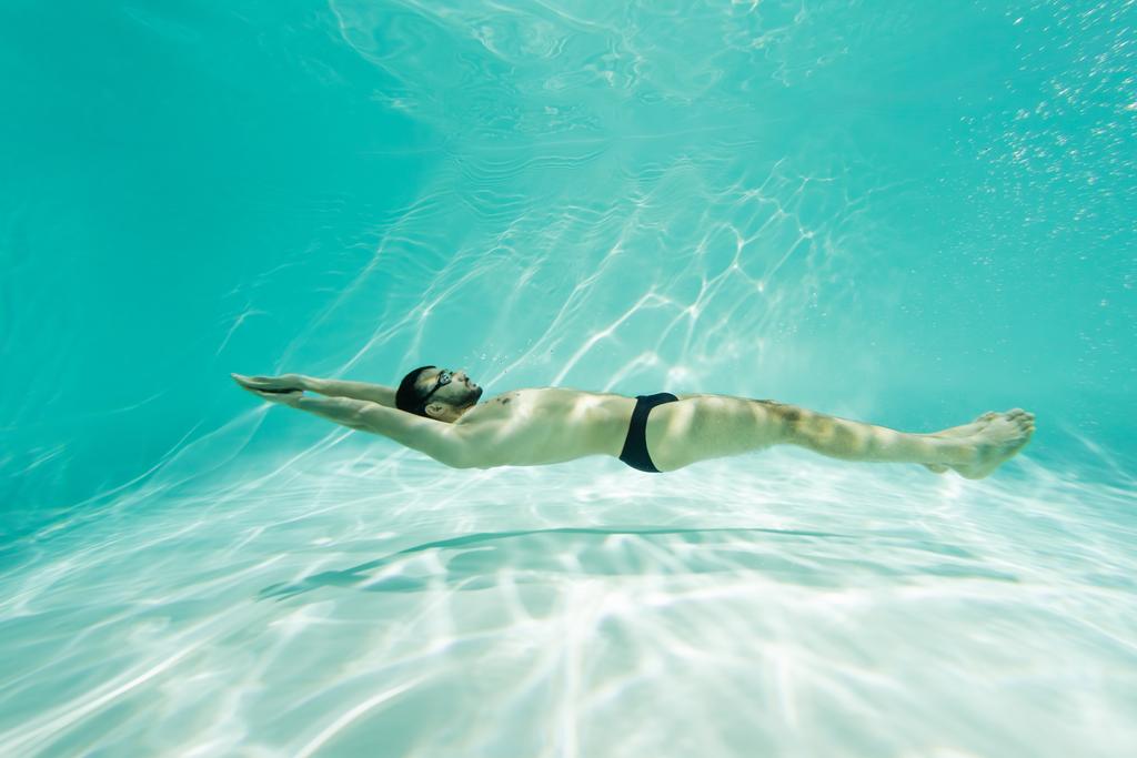 Vista lateral del nadador musulmán en baúles y gafas nadando en la piscina  - Foto, Imagen