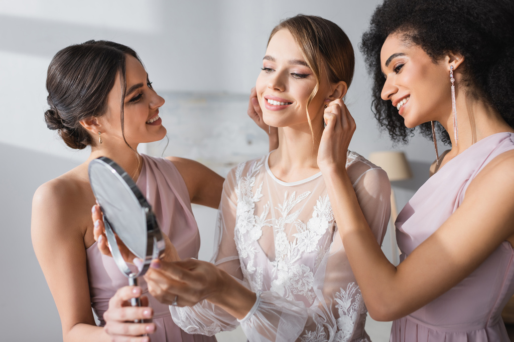young bride looking in mirror near interracial friends preparing her for wedding - Photo, Image